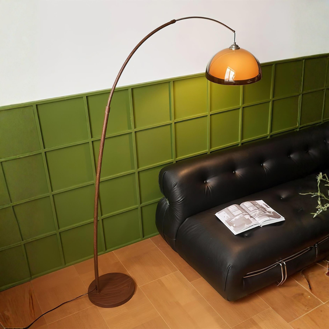 Dark brown arched floor lamp with amber dome shade over tufted leather sofa