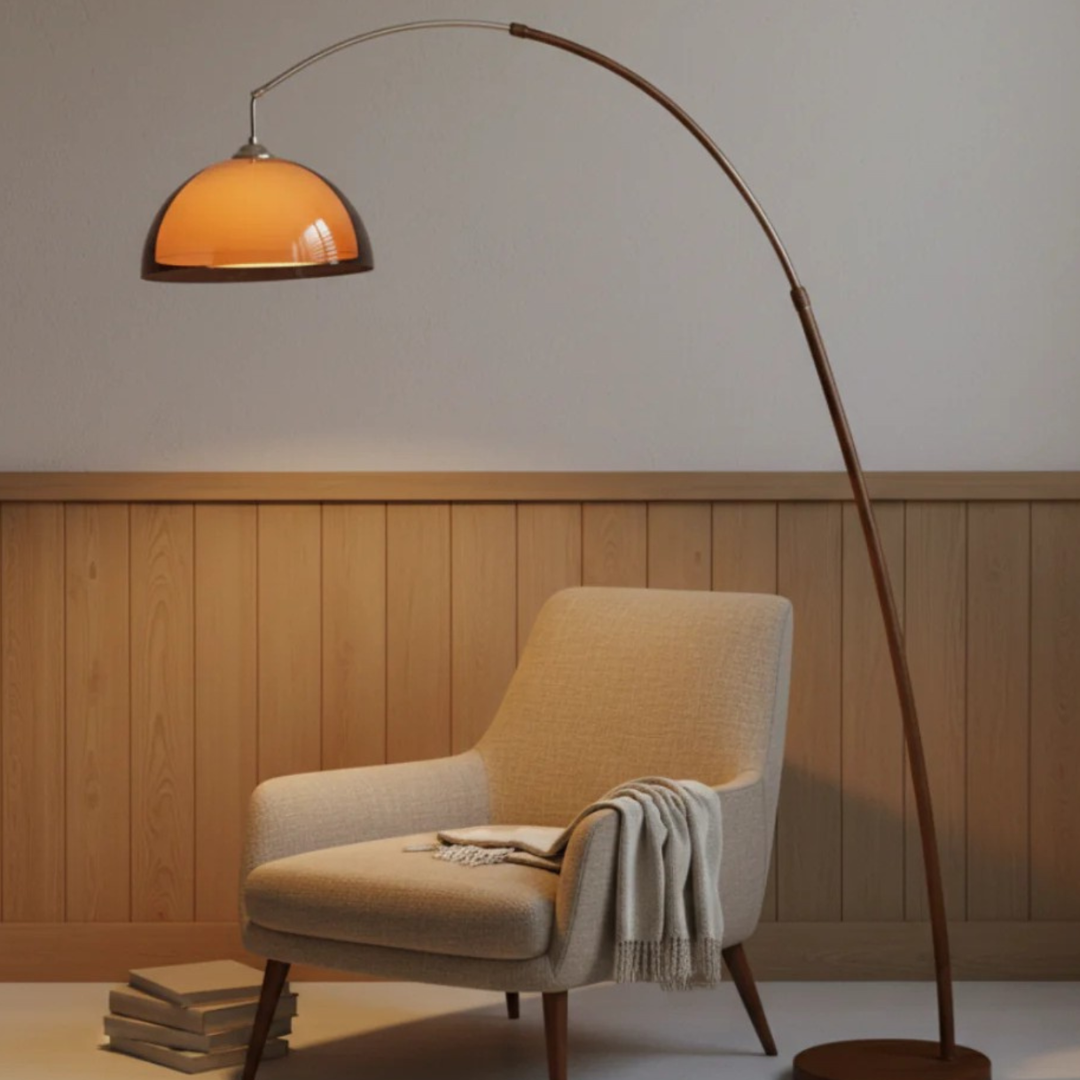 Walnut metal arc lamp with warm amber glass shade next to beige upholstered chair