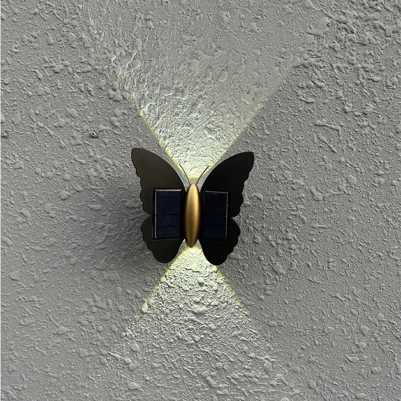 Black aluminum butterfly outdoor wall light with solar panels and warm white glow