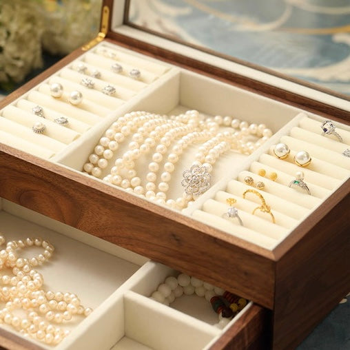 Open walnut jewelry box with glass lid, dual-layer velvet interior holding pearl necklaces and rings