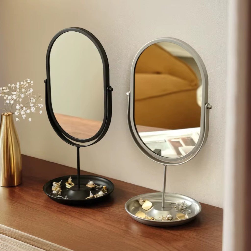 Black and silver oval desktop mirrors holding jewelry on dark wood