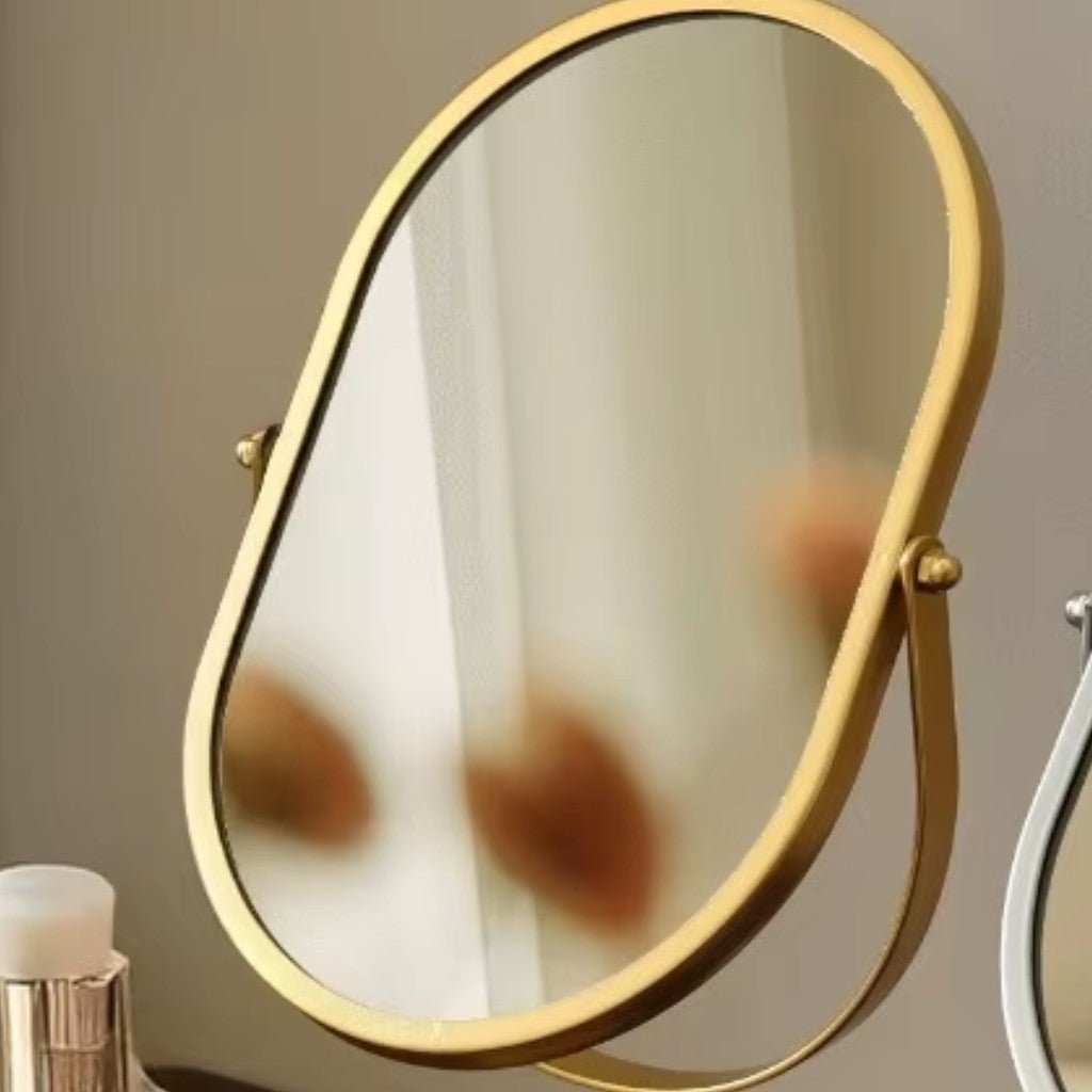 Front view of matte gold oval mirror reflecting makeup tools and hands