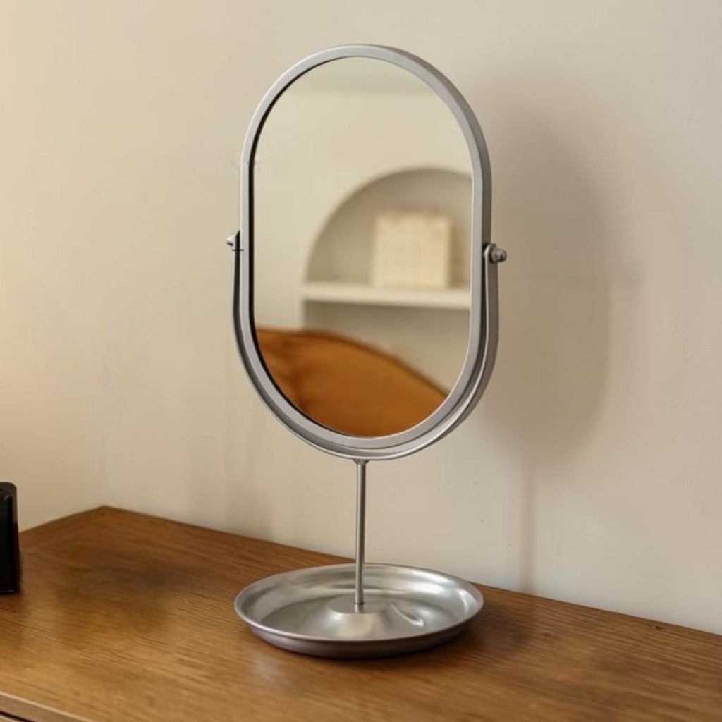 Matte silver oval vanity mirror with rotating stand on wooden surface