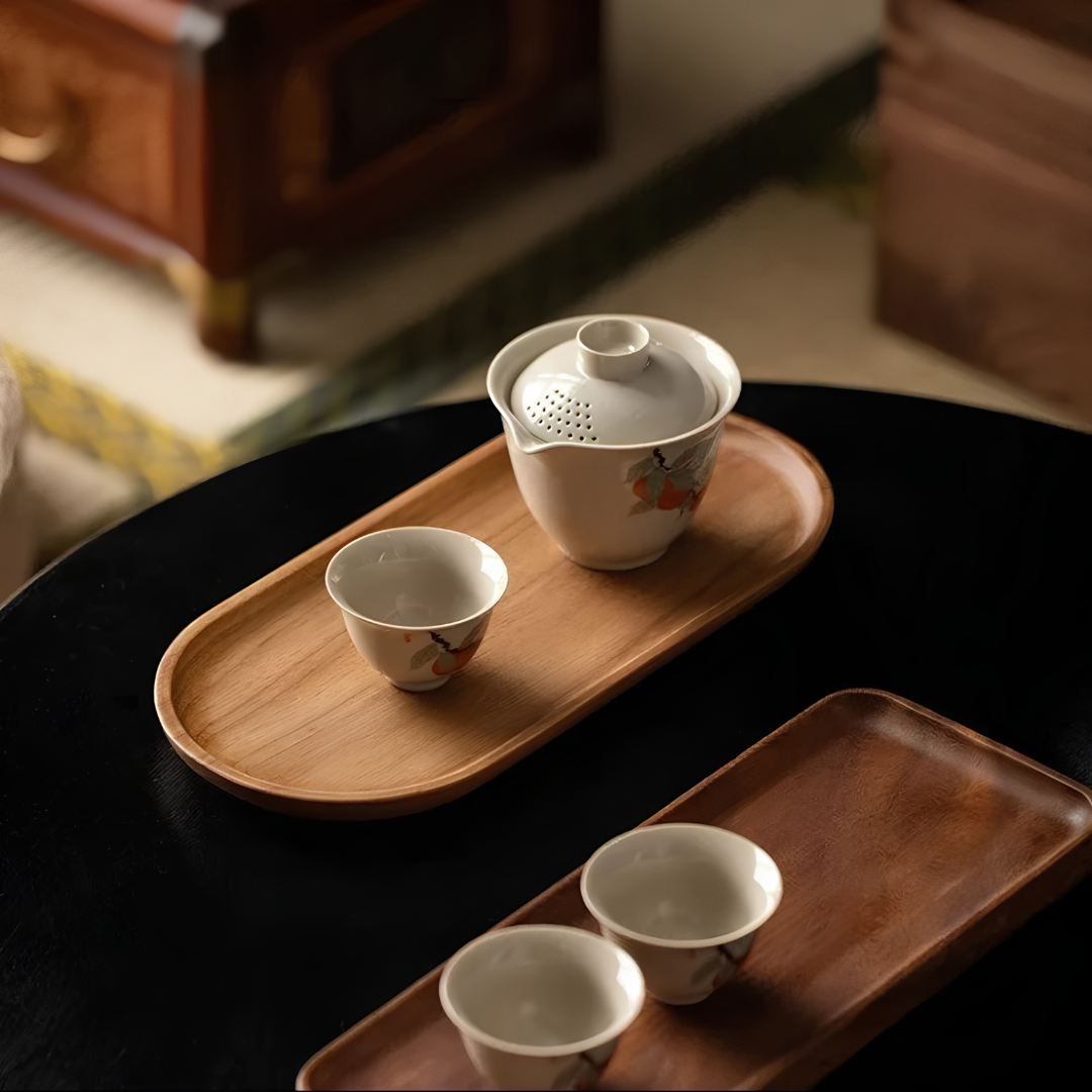 Oval walnut wood serving tray with raised edge holding hand-painted persimmon ceramic tea set