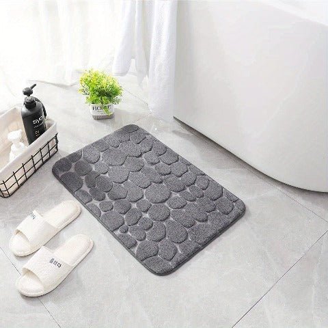 Gray 3D cobblestone bath rug beside white tub with slippers nearby
