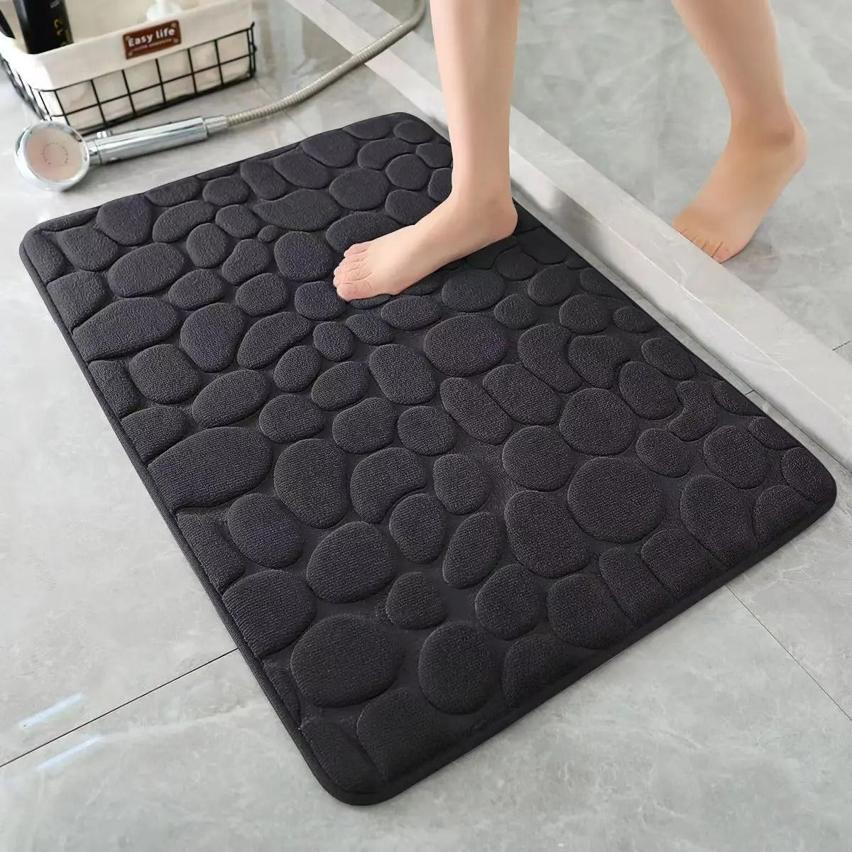 Black cobblestone bath mat with non-slip rubber backing on tiled floor