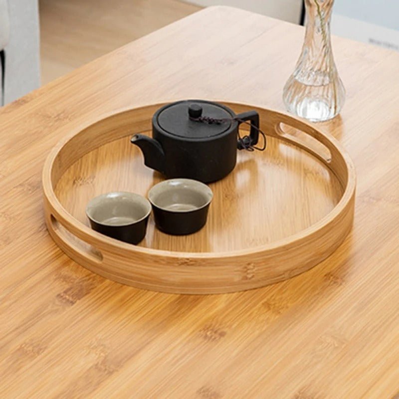Round bamboo serving tray holding black ceramic teapot and cups for modern home entertaining