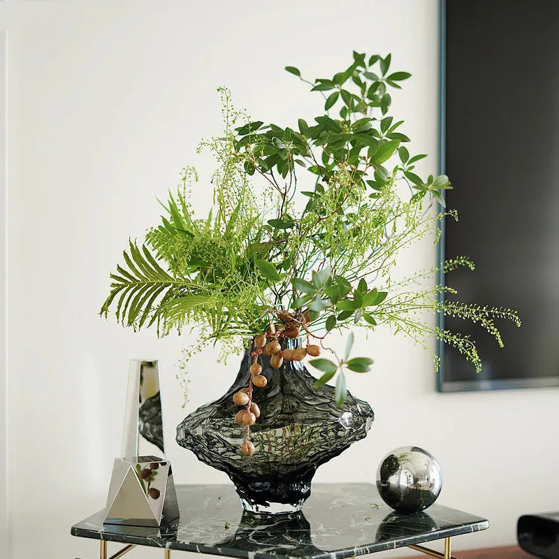 Smoky gray rippled glass vase with organic design holding green ferns and berries