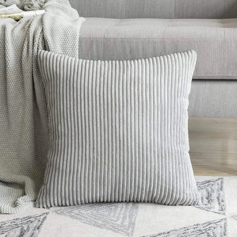 Light gray ribbed corduroy pillow case on geometric rug with sofa backdrop