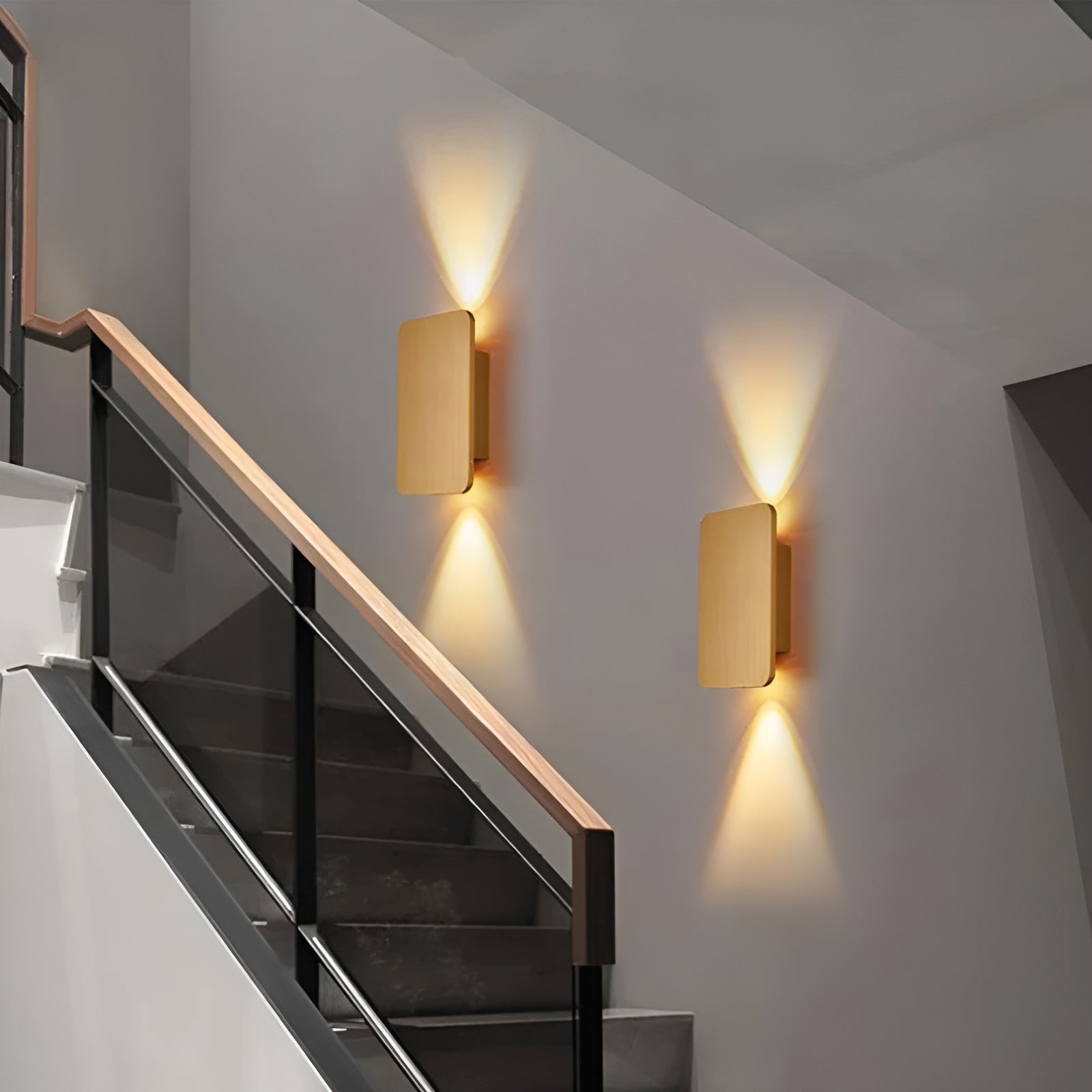 Pair of gold-finished rectangular wall sconces beside glass-paneled staircase