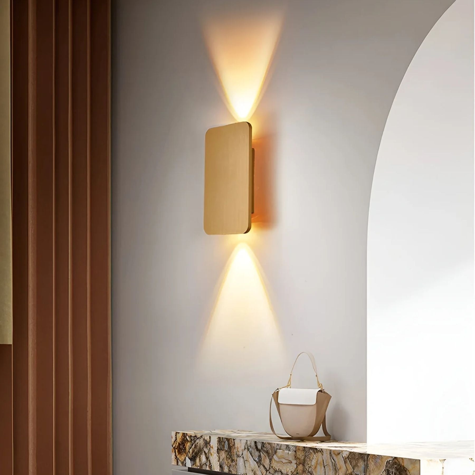 Gold rectangular wall sconce illuminating marble console table near arched doorway