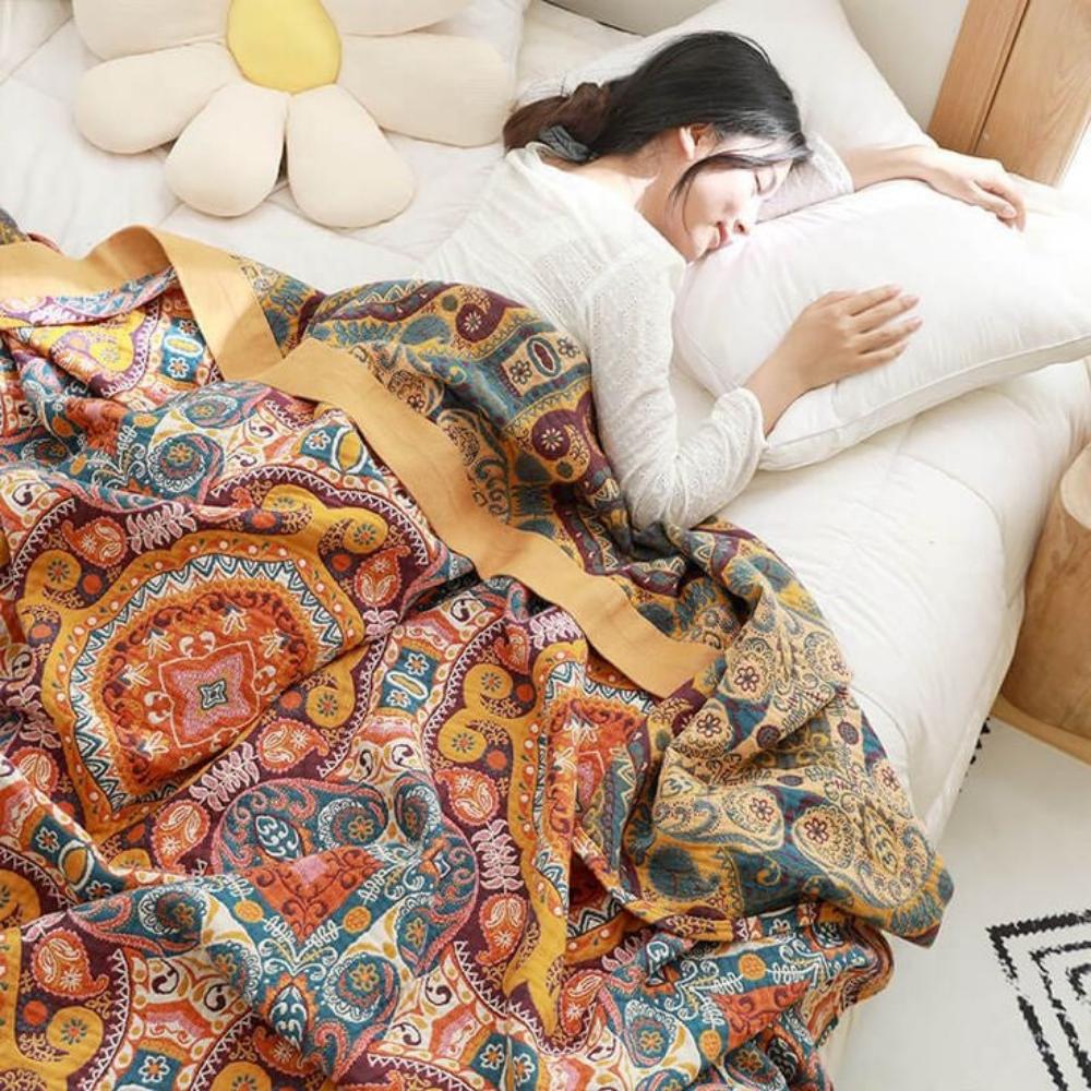Sunrise Boho Reversible Blanket with paisley mandala pattern in orange teal maroon on bed