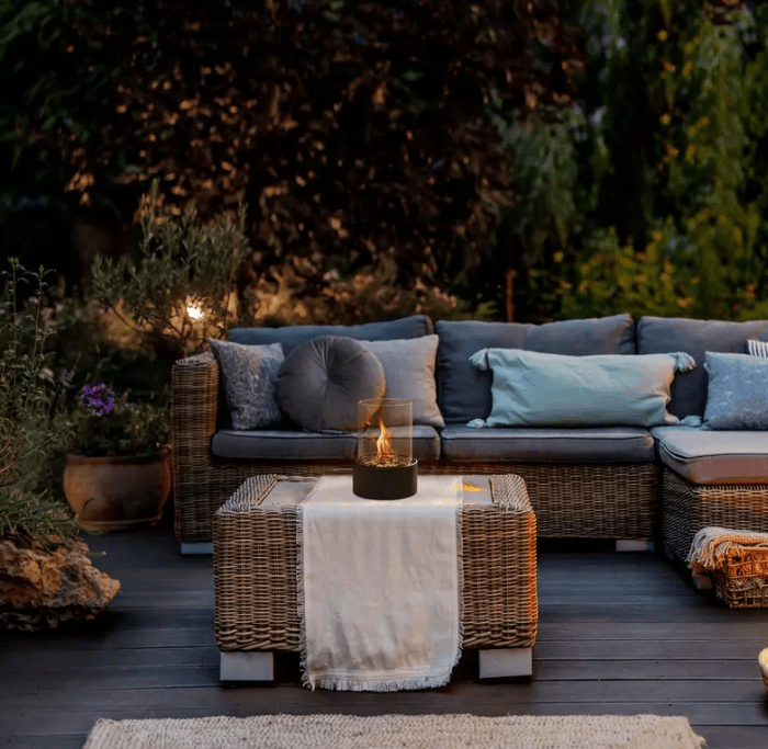 Black concrete tabletop fireplace on wicker coffee table at dusk
