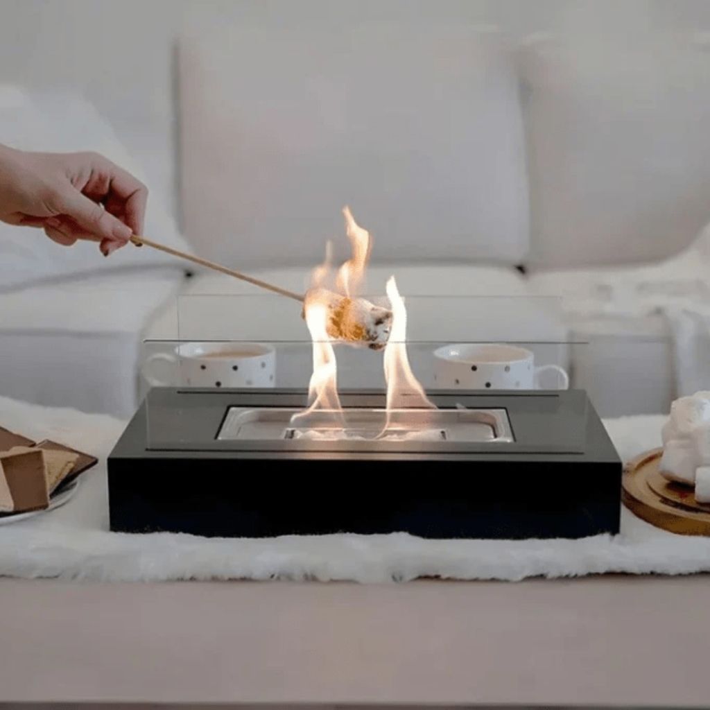 Hand toasting marshmallow over active flame in glass-enclosed indoor fire pit
