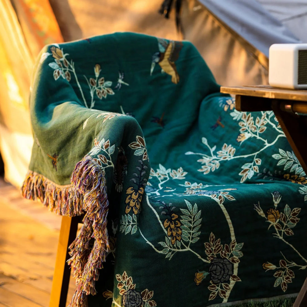 Green reversible cotton throw blanket with floral vines and fringe on wooden chair