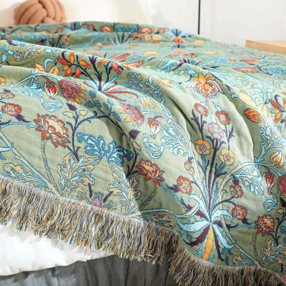 Green vintage floral blanket with multicolored fringe draped over white bed