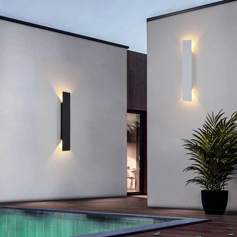 Black weatherproof LED wall light illuminating poolside patio at dusk