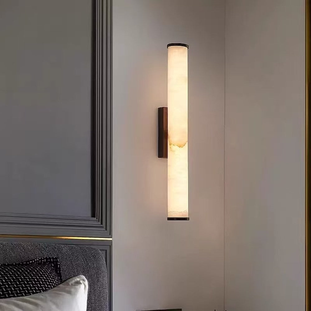 Maintained House Marble Tube Wall Sconce - Lit beside a bed in a bedroom corner