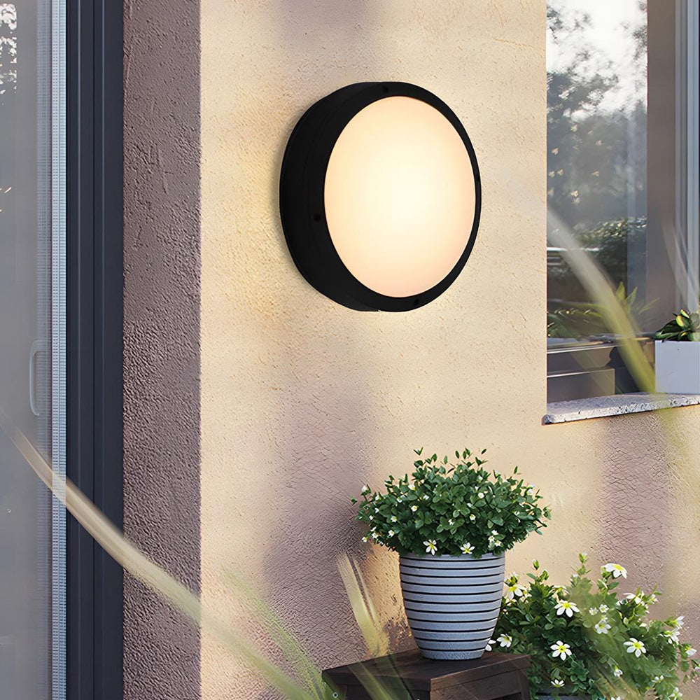 Maintained House Round Outdoor LED Wall Light - Plain style on a beige wall beside potted plants